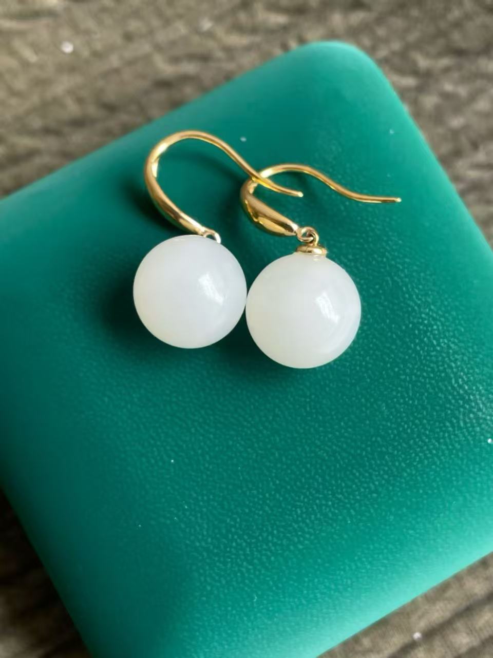 HeTian jade White round earrings with gold hooks on a green surface
