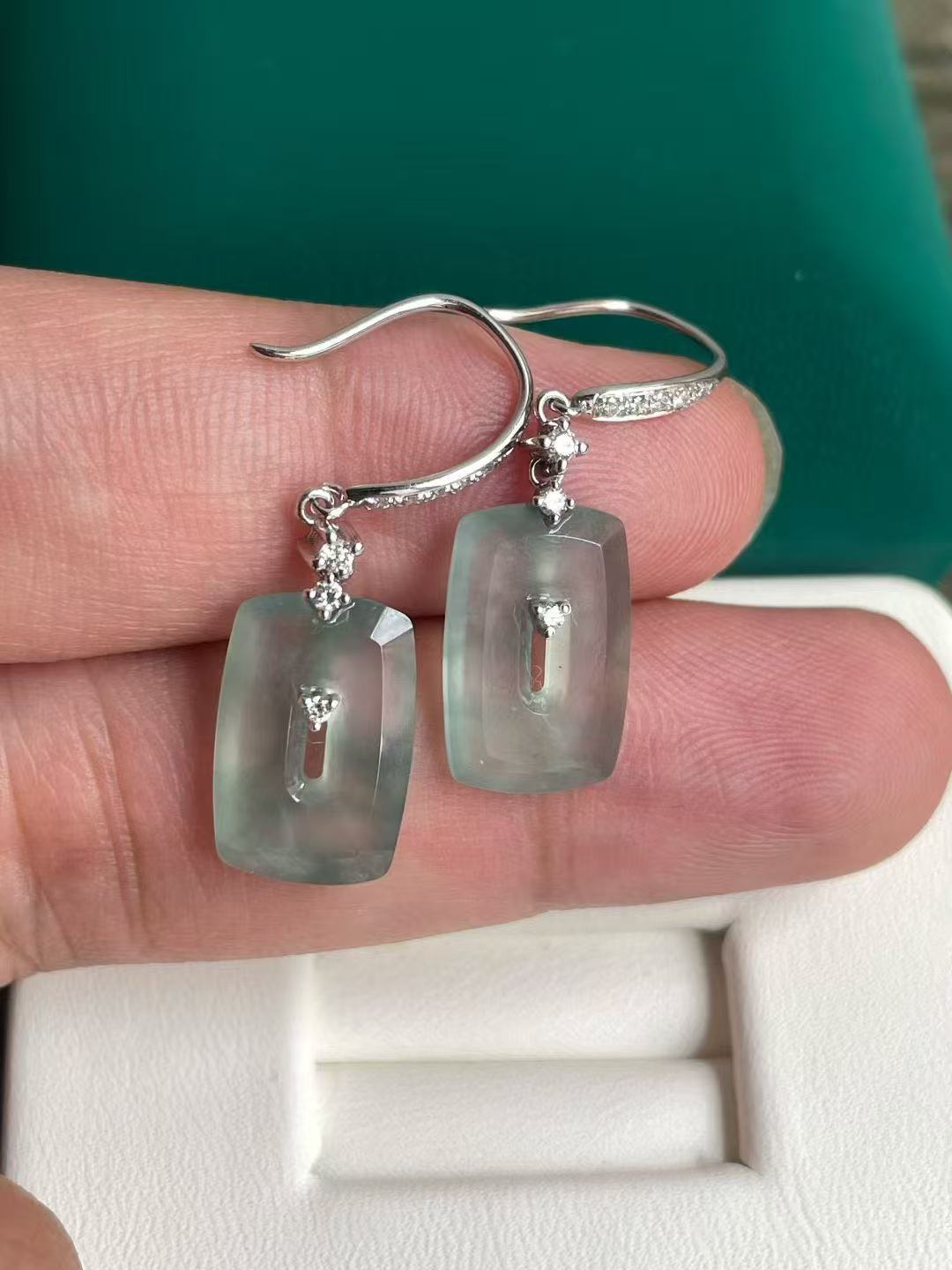 Jade earrings with clear stones held between fingers against a green background