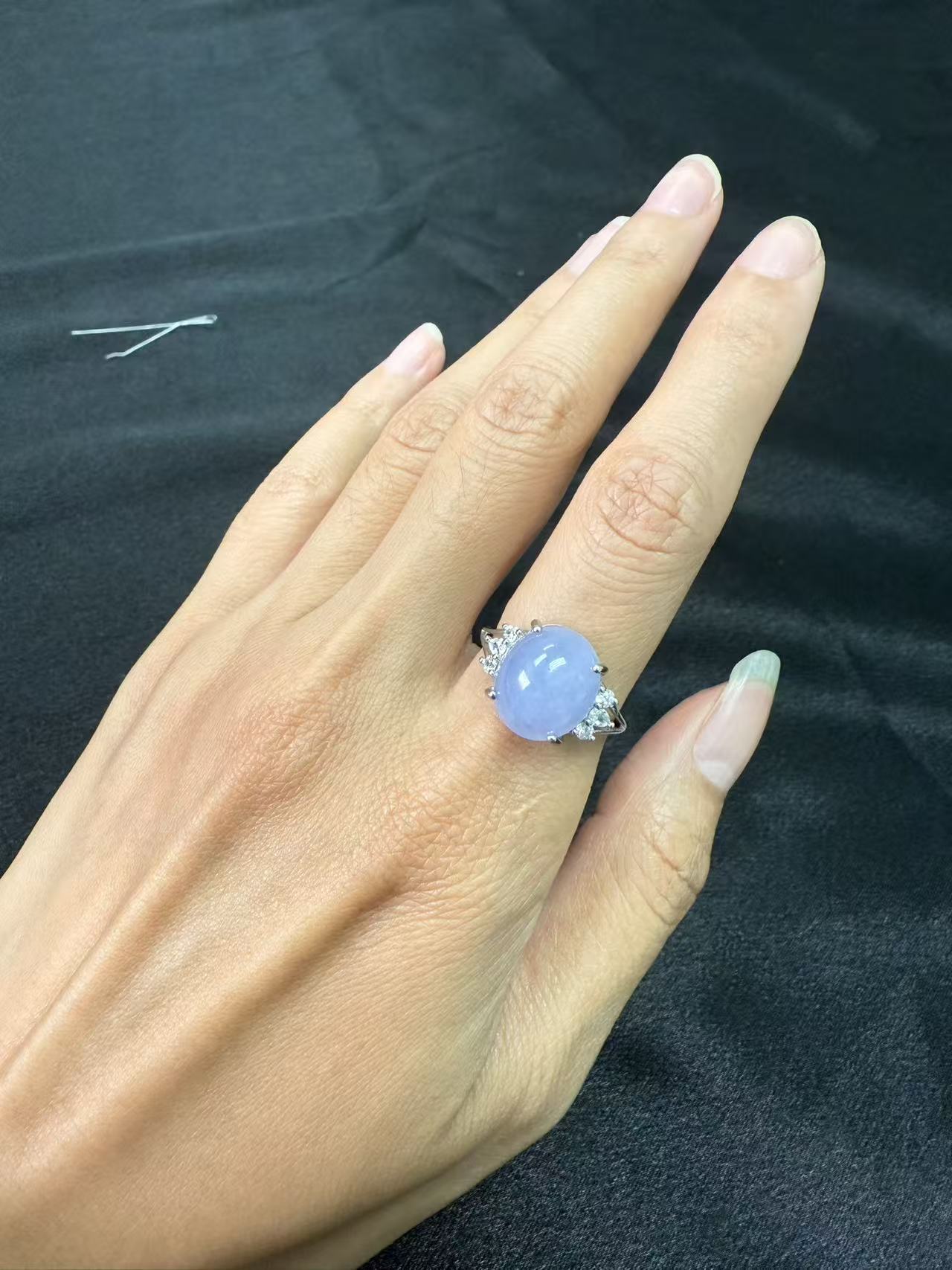 Hand wearing a jadeite ring with s925 silver band and a dark fabric background