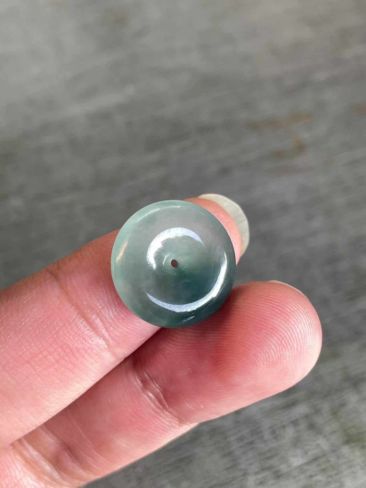 Green jade bead held between fingers against a gray background