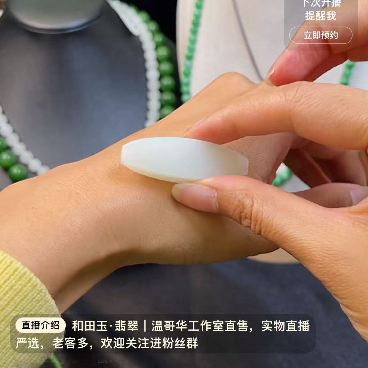 Sylvia Jewelry white jade pendant being held against a wrist, with jade necklaces in the background.