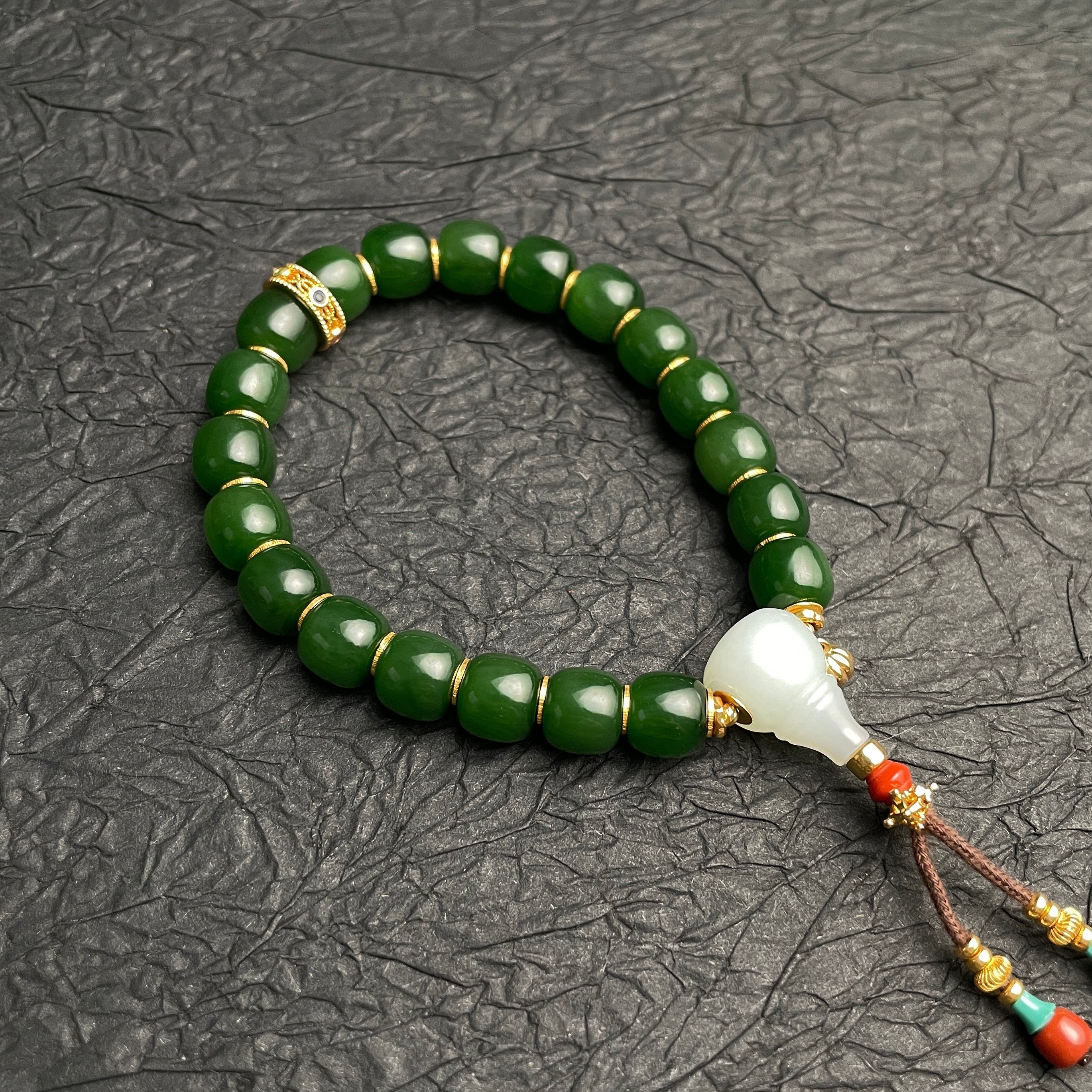 Green beaded bracelet with a white and gold tassel on a textured gray background