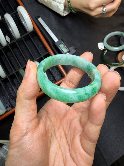 Hand holding a green jadeite bagel with a blurred background of more rings and jadeite.