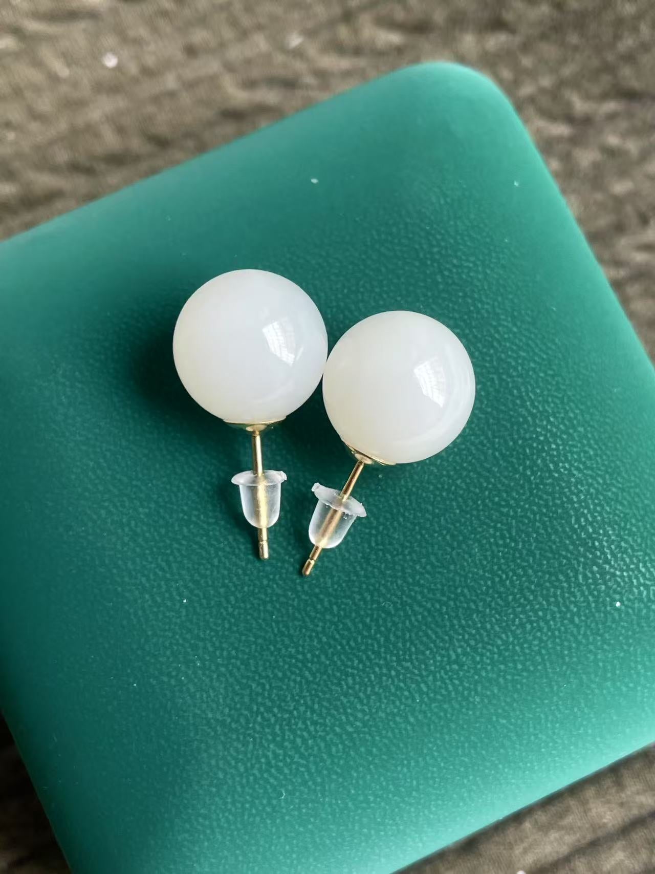 White spherical HeTian jade earrings on a green surface