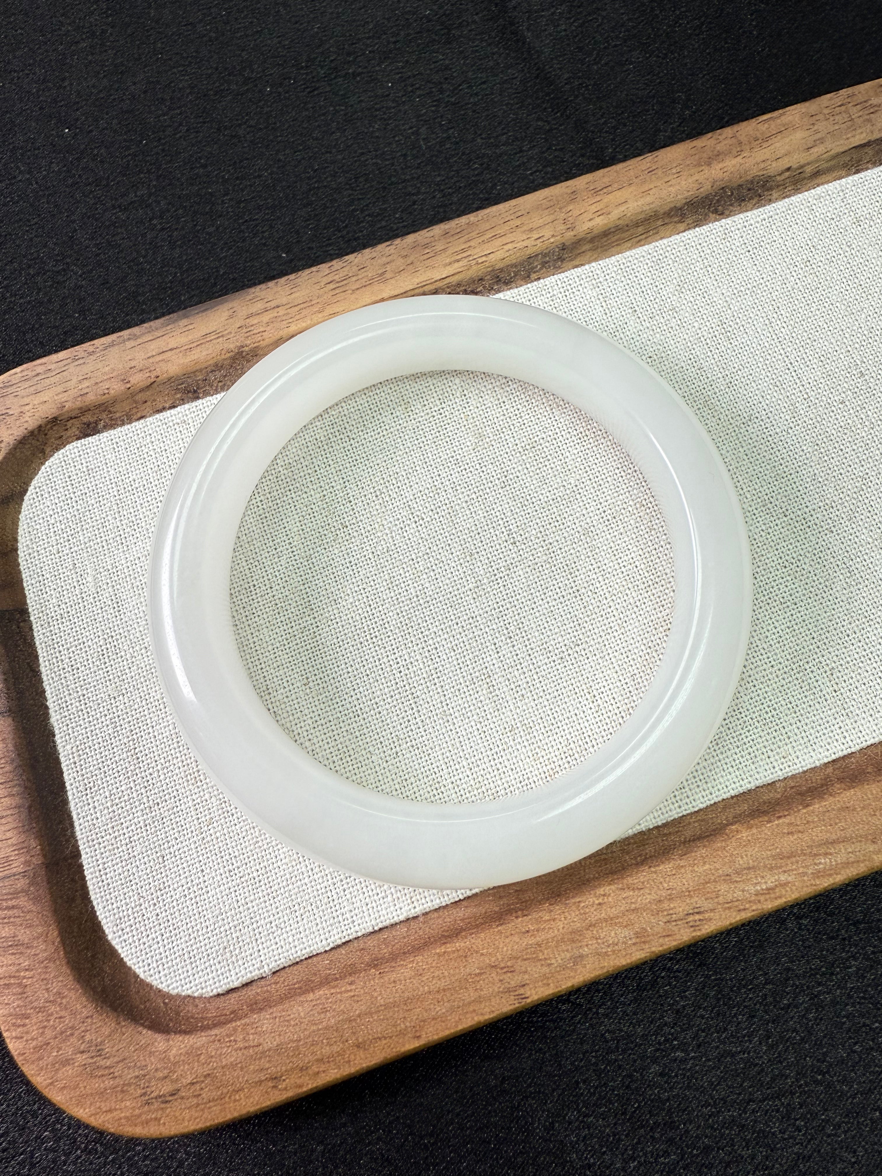 White jade HeTian bangle on a wooden tray with a black background
