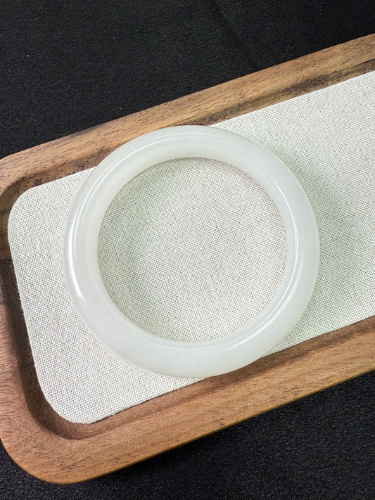 White jade HeTian bangle on a wooden tray with a black background