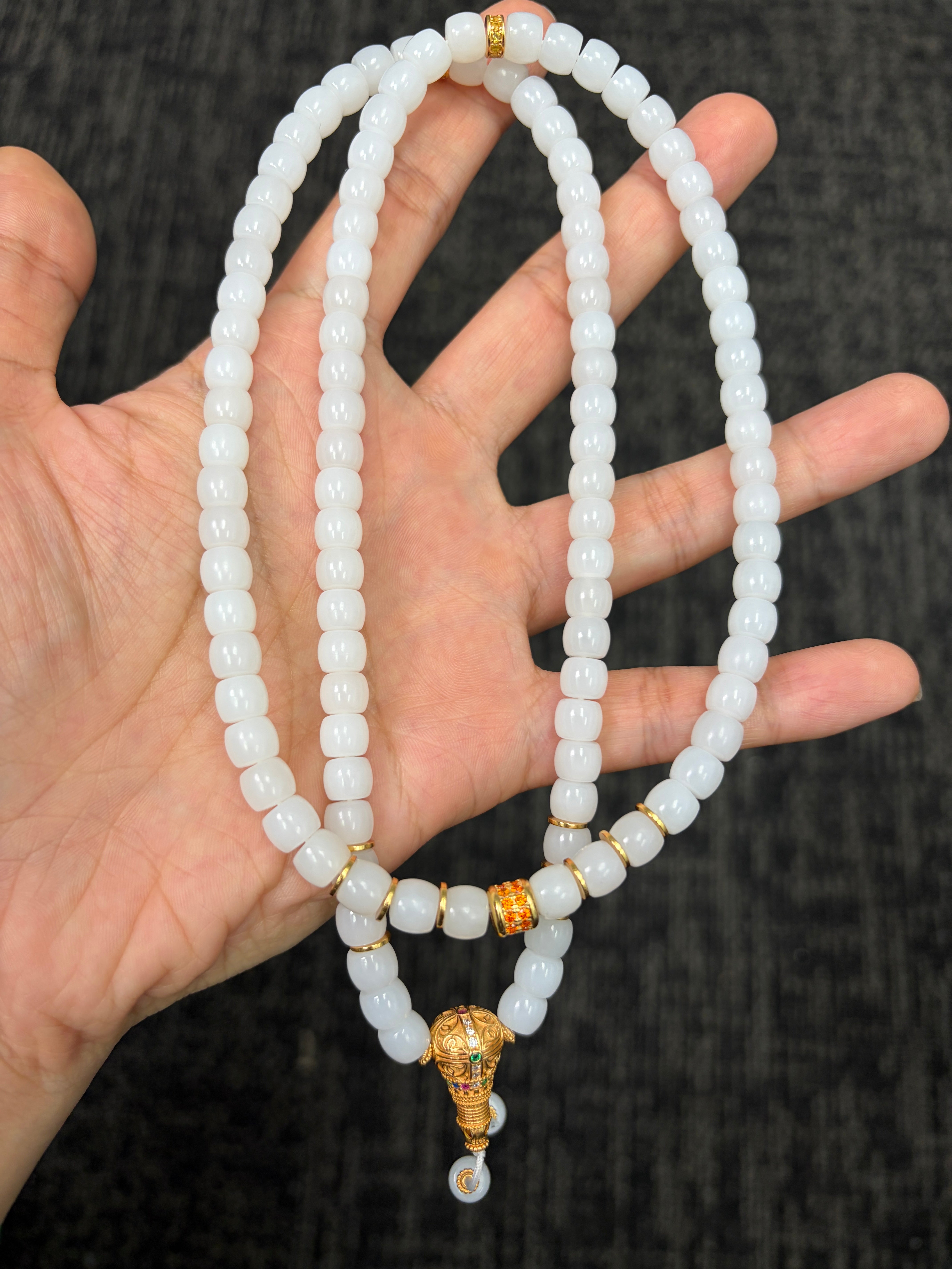 White HeTian jade beaded necklace with gold colour clasps on a hand against a dark background