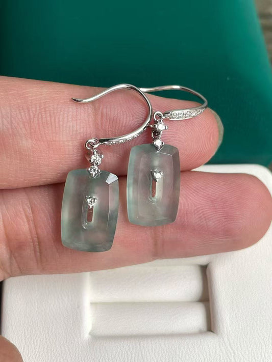 Jade earrings with clear stones held between fingers against a green background