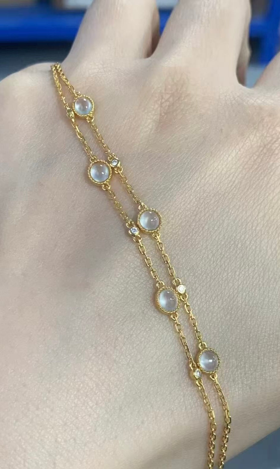 Gold bracelet with jade on a hand against a neutral background