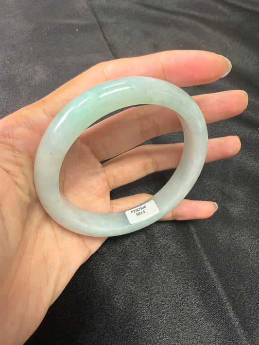 Hand holding a light green jade bracelet against a dark background