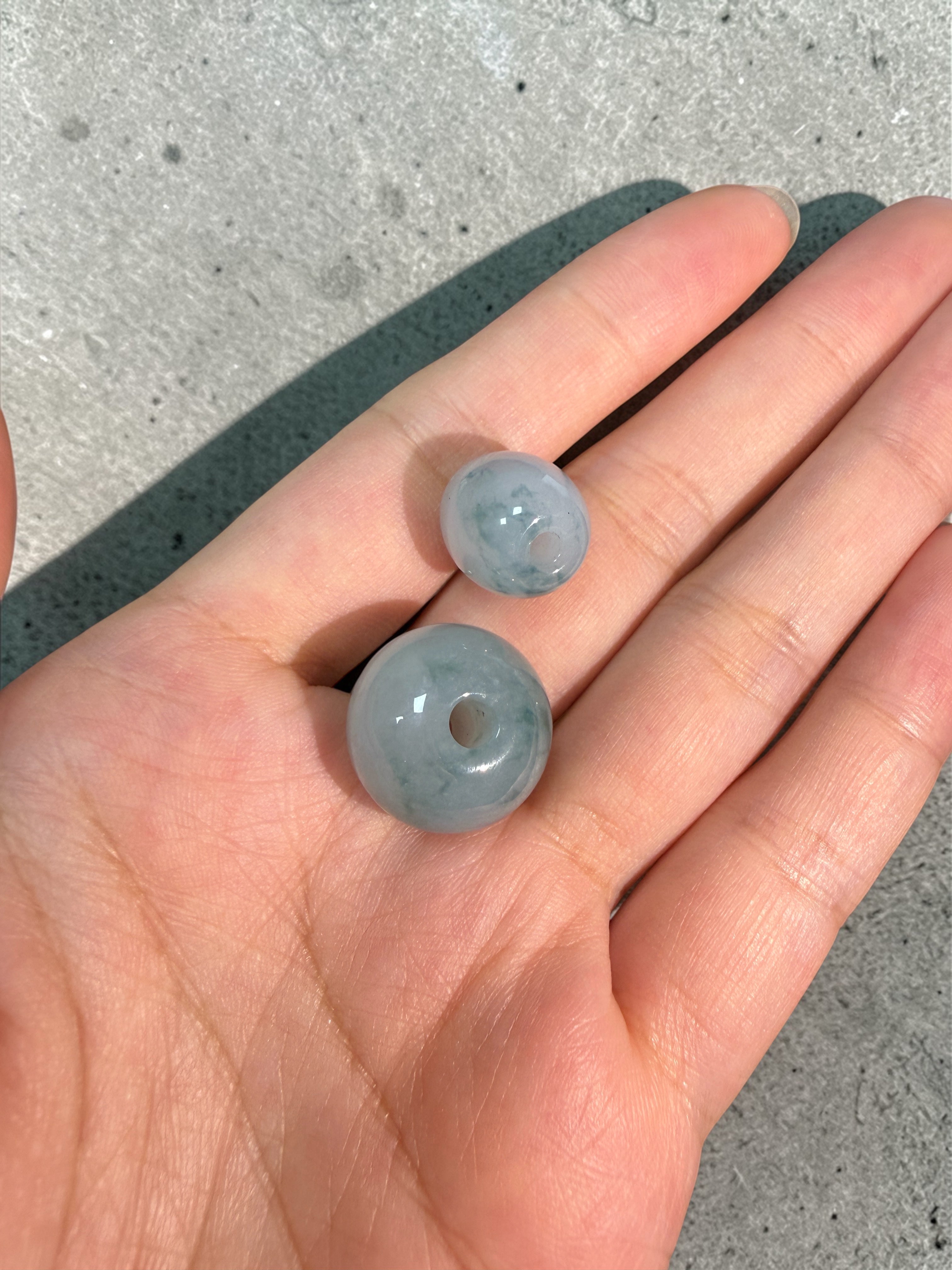 Two gray beads held in a hand against a concrete background