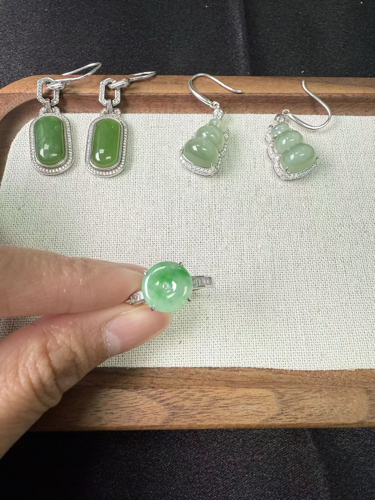 Set of jade jewelry including earrings and a ring on a textured surface.