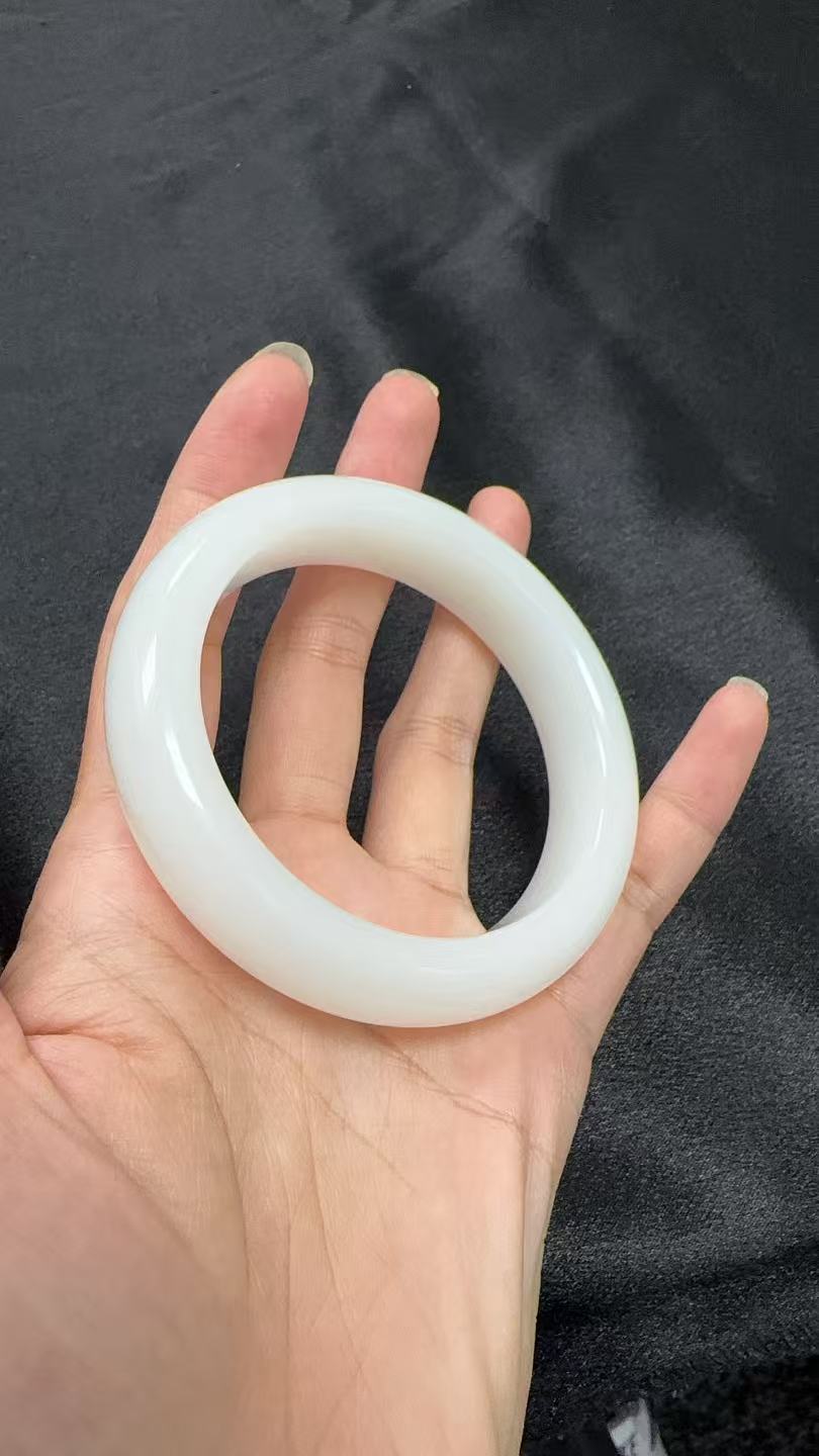Hand holding a white HeTian white jade bracelet against a dark background