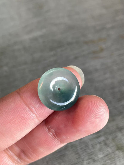 Green jade bead held between fingers against a gray background