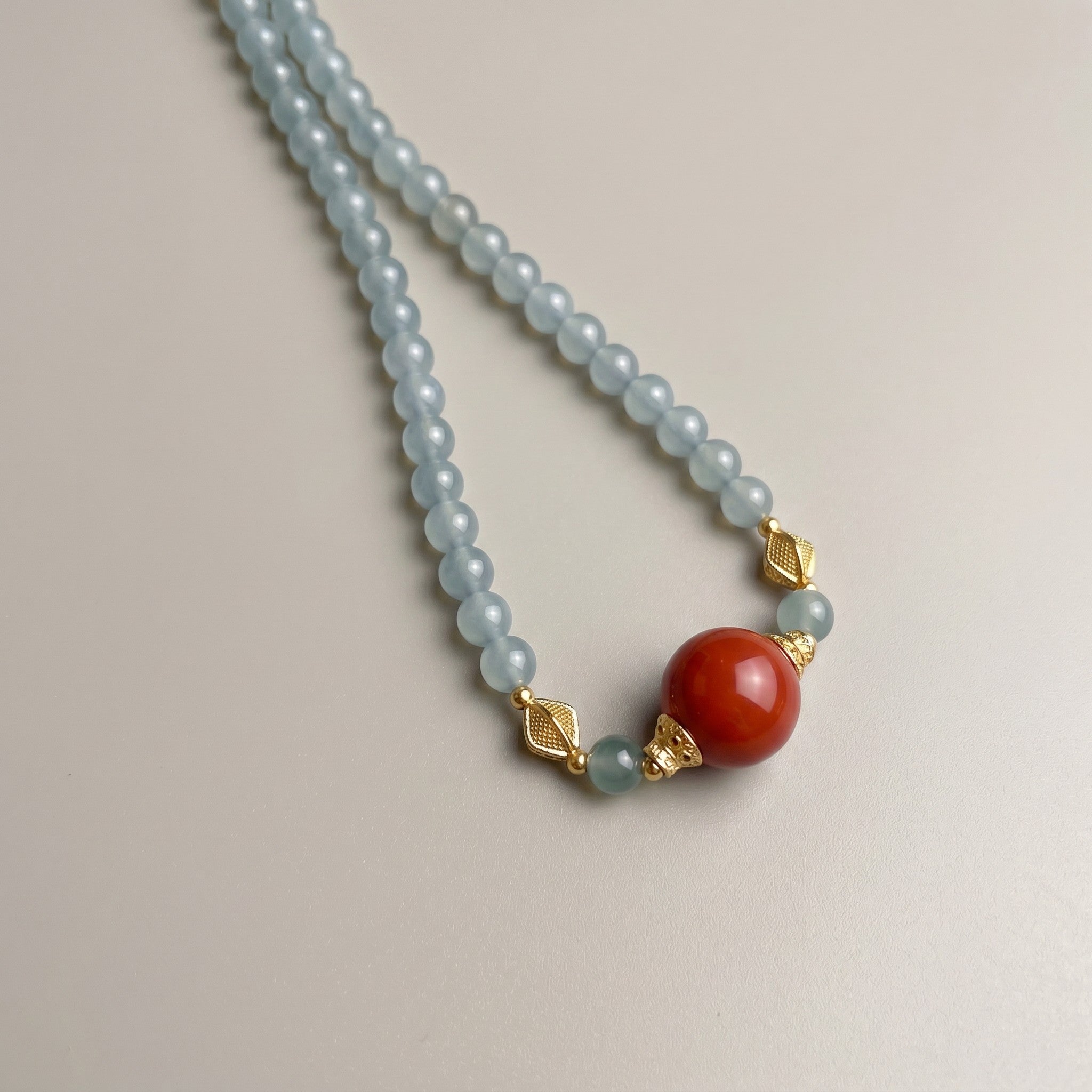 Sylvia Jewelry 浅蓝色串珠项链，镶嵌一颗醒目的橙红色圆形宝石，搭配金色菱形隔珠。