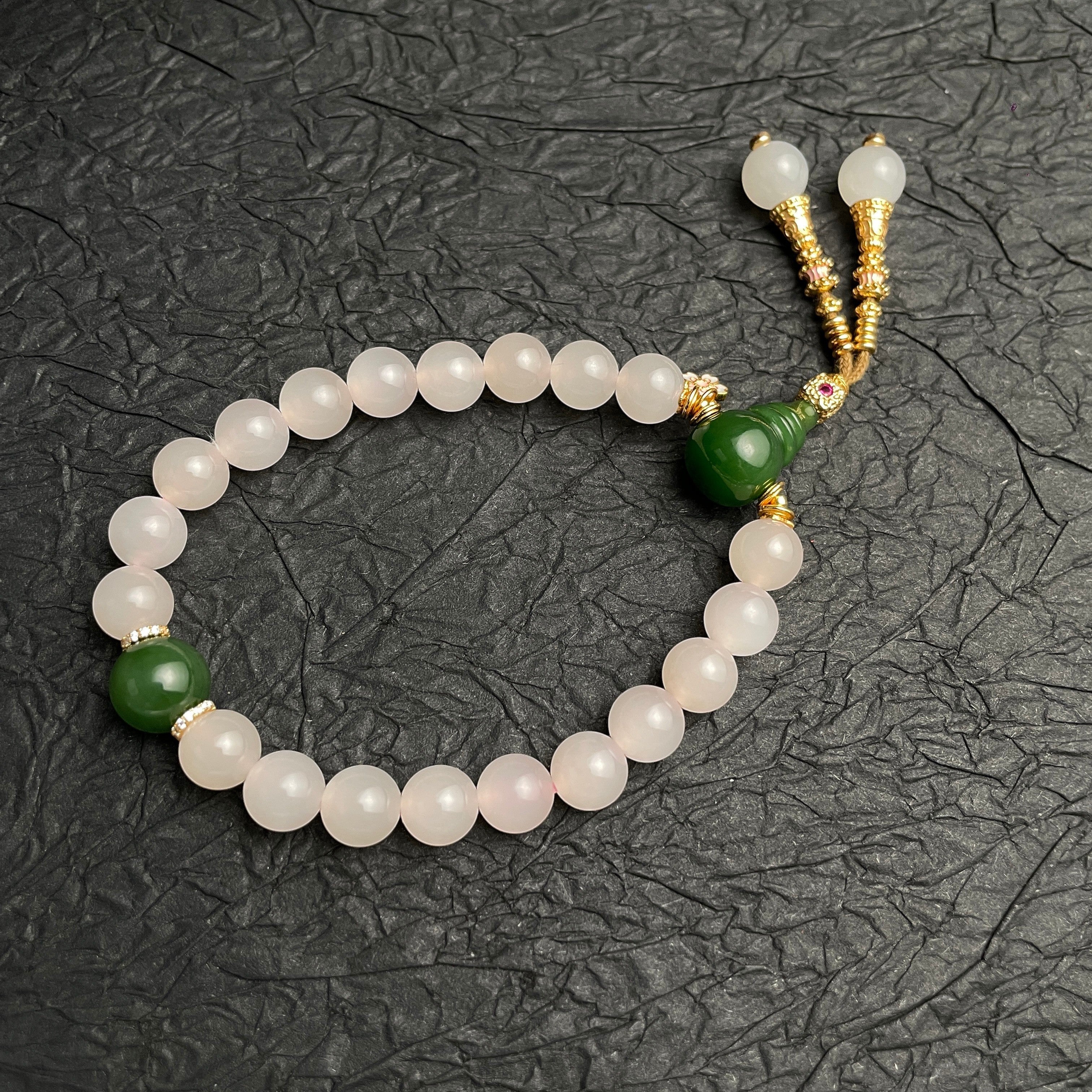 Sylvia Jewelry 粉色水晶串珠手链，搭配绿色玉石吊坠和金色流苏装饰。